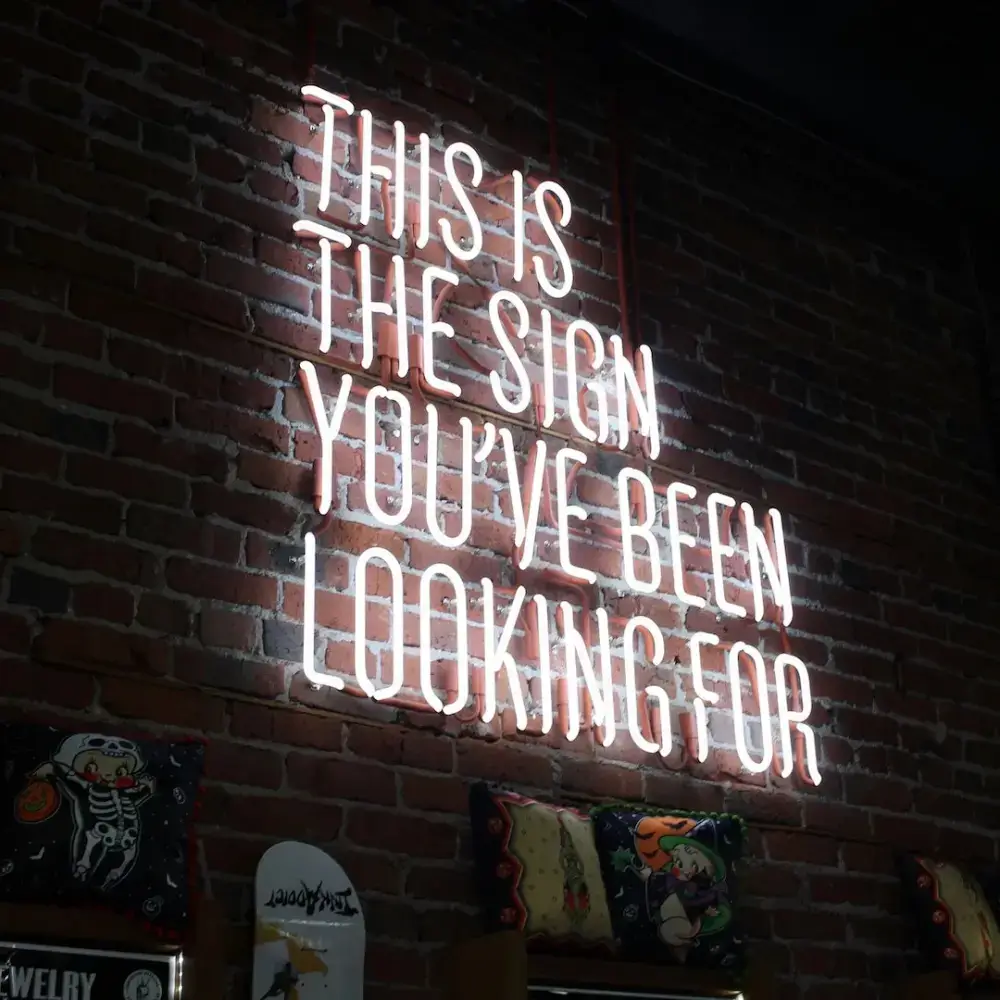 White glass neon quote sign mounted on an exposed brick wall
