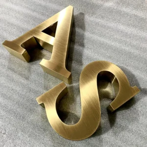 Brushed antique bronze dimensional letters A and S on textured gray surface