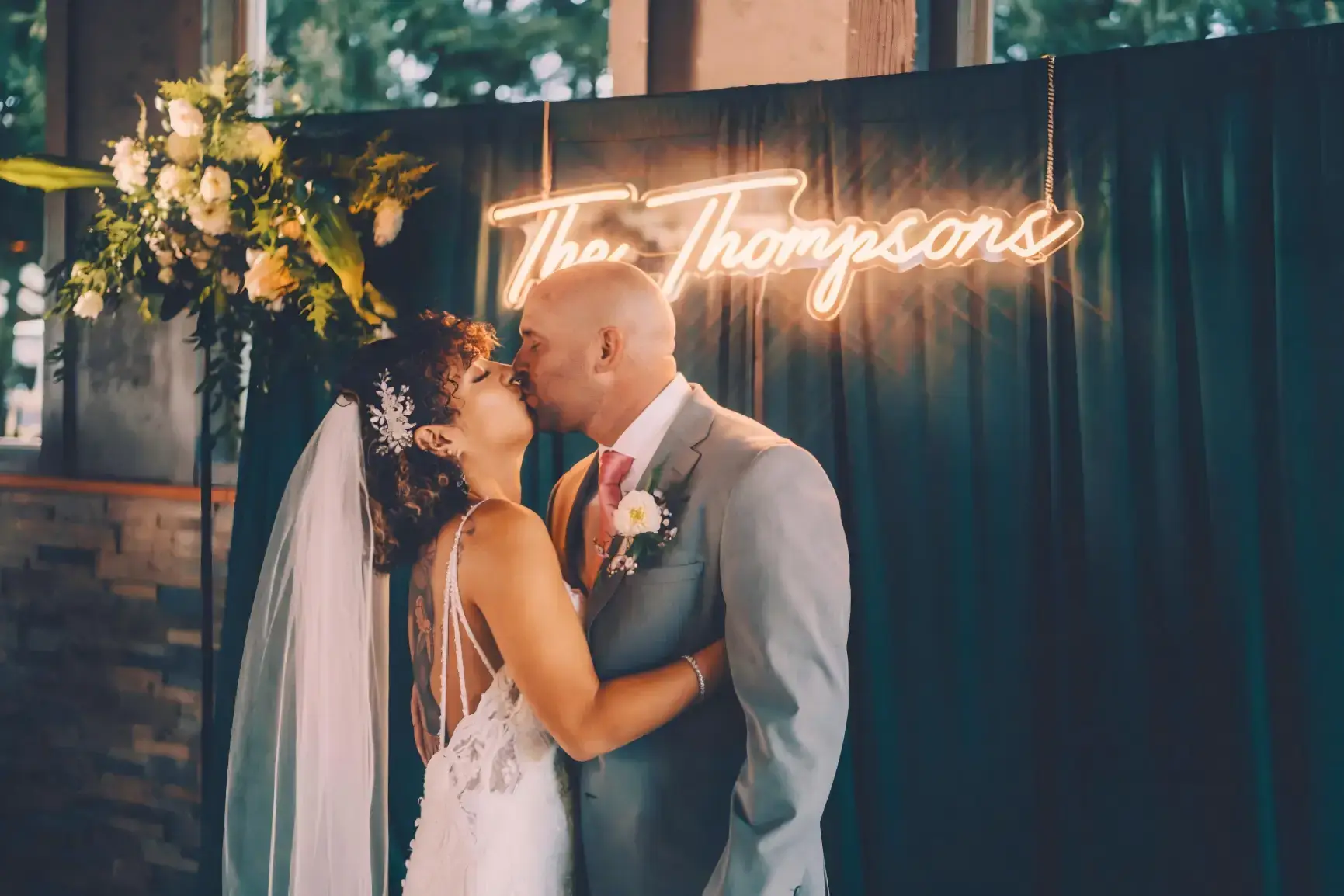 Newlywed couple beneath a warm white custom surname neon sign