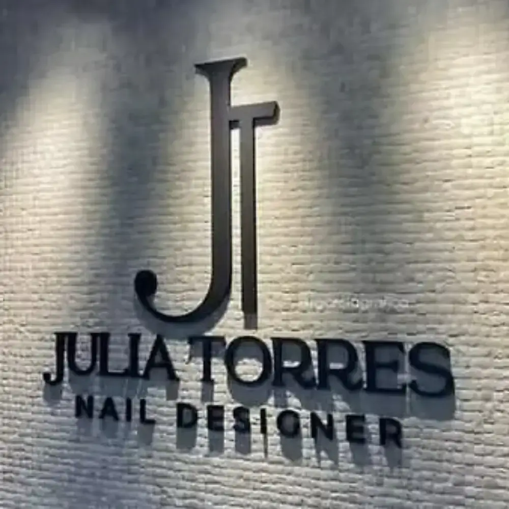 Black Julia Torres Nail Designer acrylic letters and JT monogram on a textured wall