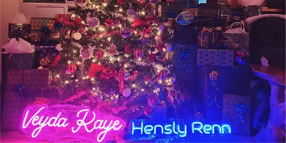 Two custom name neon signs displayed beside a decorated Christmas tree