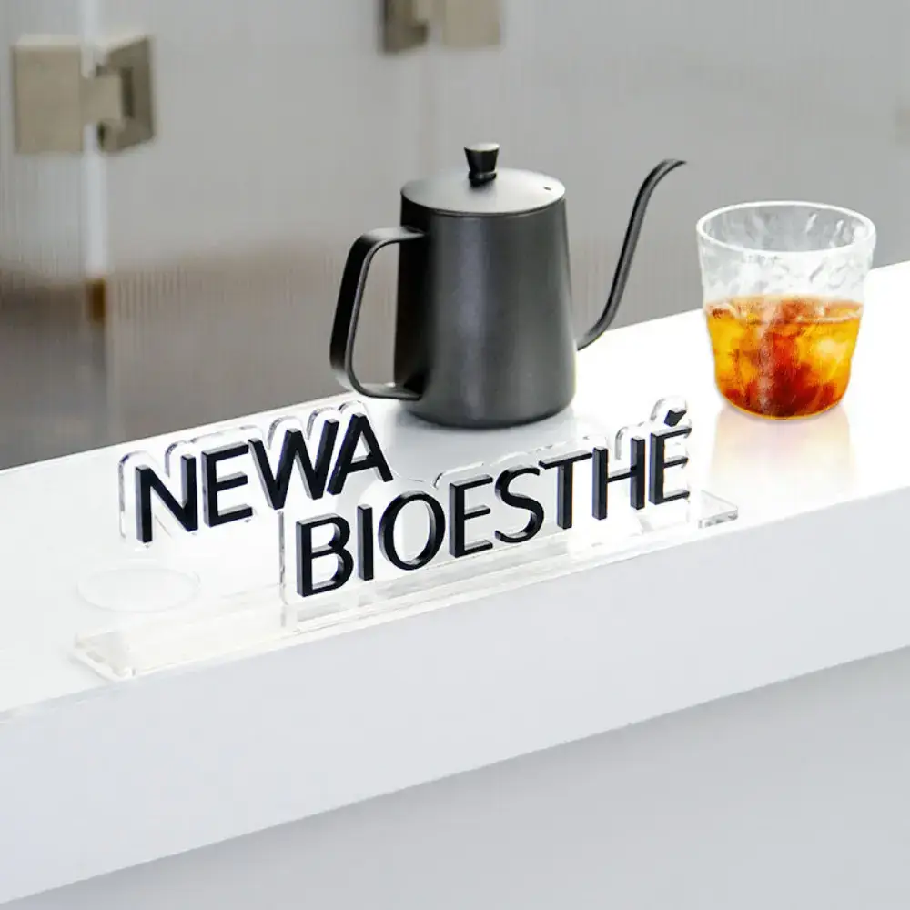 Freestanding clear acrylic NEWA BIOESTHÉ letters with black faces on a white countertop