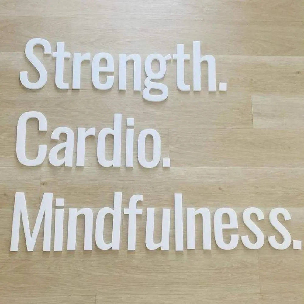 White acrylic words Strength Cardio and Mindfulness mounted on a wood-effect wall