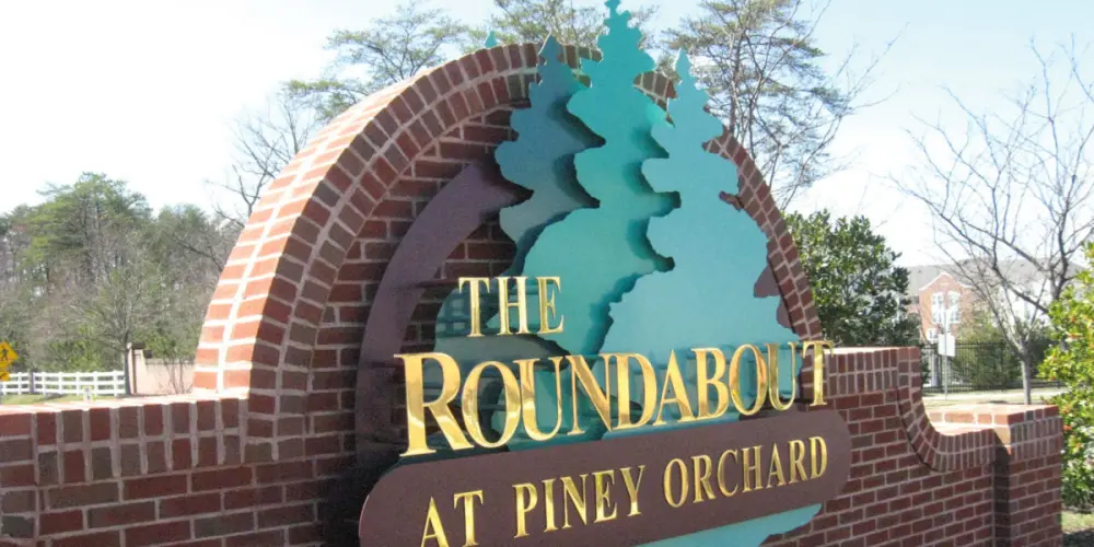 The Roundabout at Piney Orchard brick monument sign with gold lettering and teal tree design
