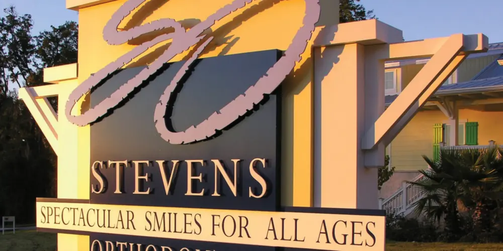 Stevens Orthodontics pylon sign with pink script logo and dimensional letters at sunset