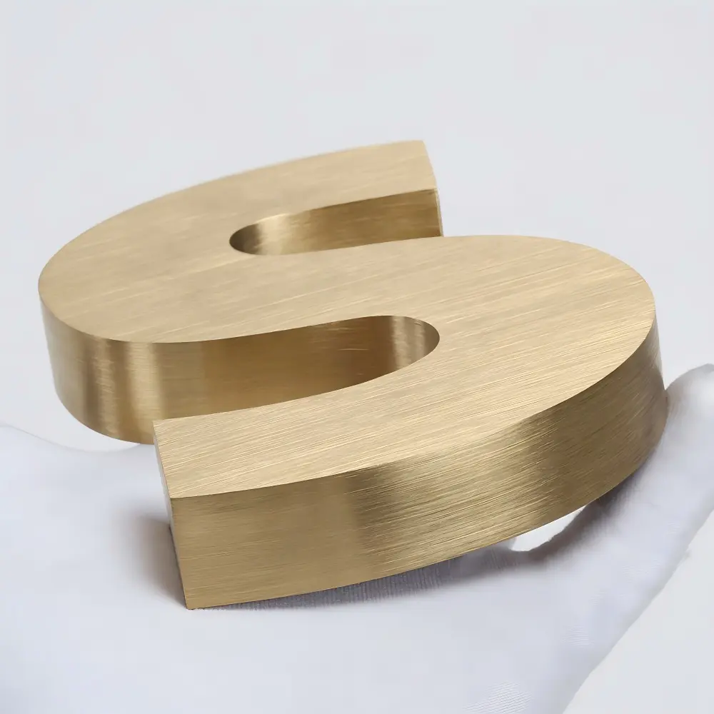 Brushed gold dimensional letter S resting on white fabric close-up