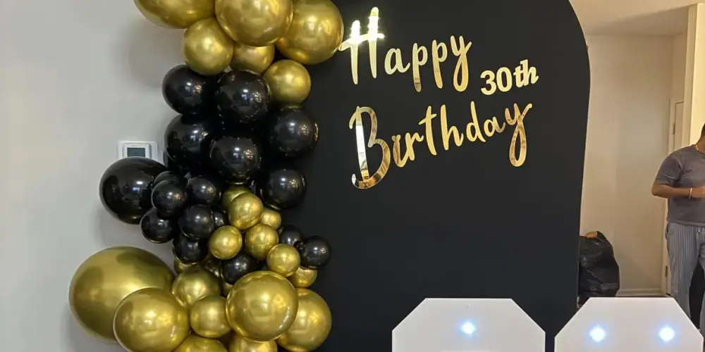 Gold mirror acrylic Happy 30th Birthday lettering on a black backdrop with black and gold balloons