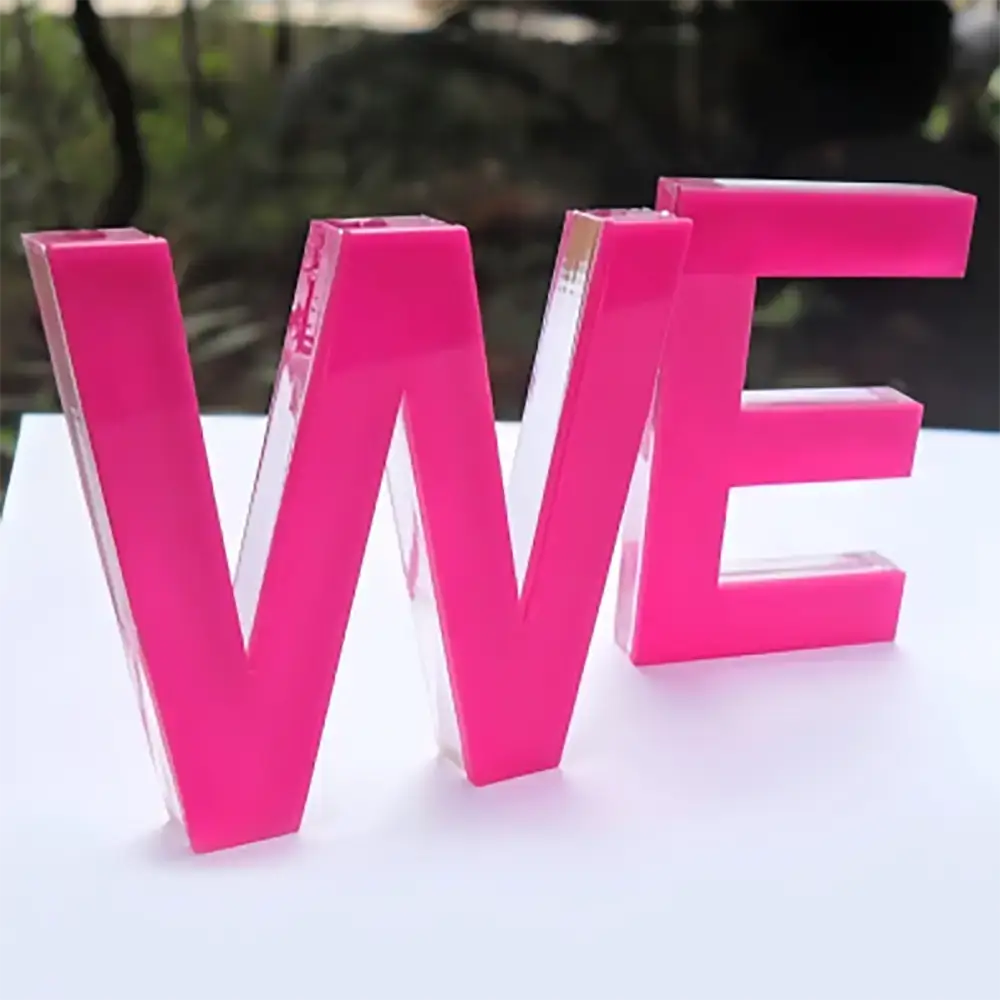 Freestanding pink W and E acrylic letters with clear edges on a white surface