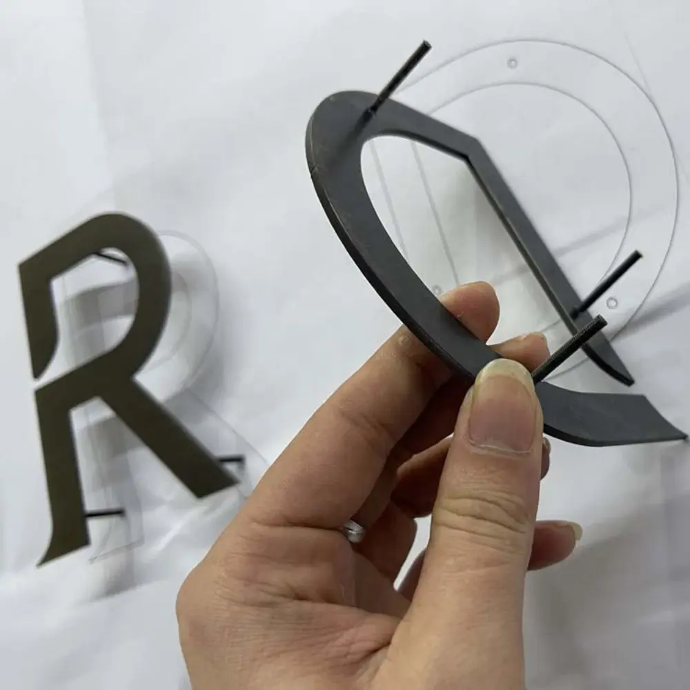 Hand holding black acrylic letter Q next to letter R with printed template underneath