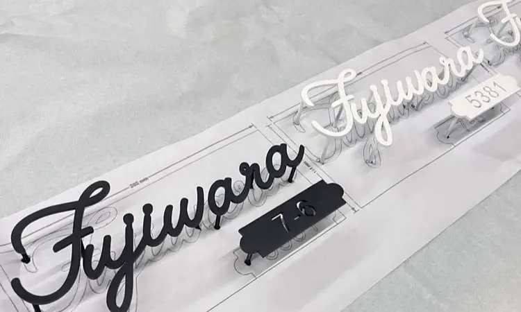 Black and white acrylic script letters spelling "Fujiwara" laid over printed design template