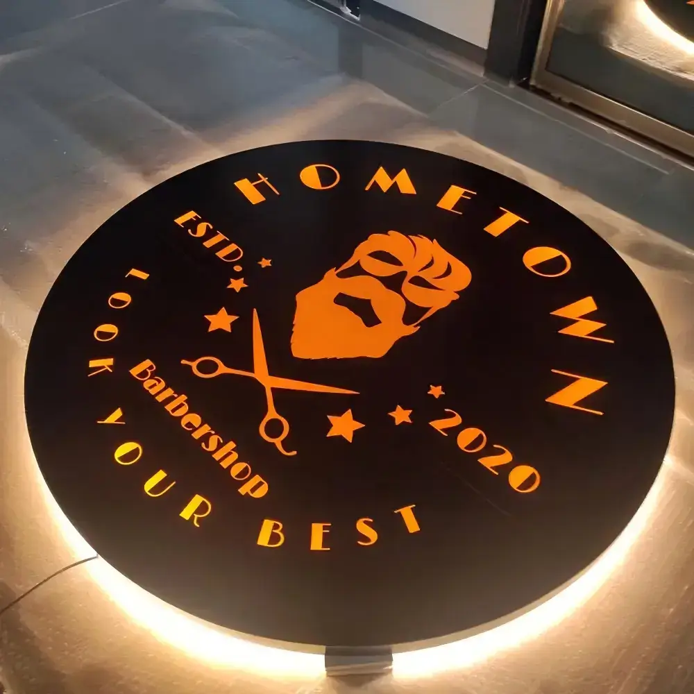 Round illuminated light box with a laser-cut black metal face panel and warm backlighting