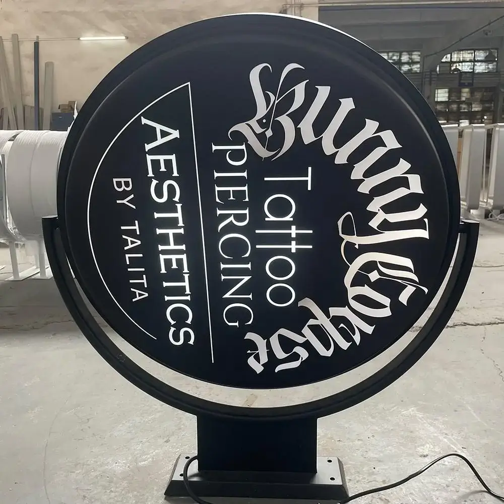 Large circular black rotating light box in a freestanding frame with white tattoo studio graphics