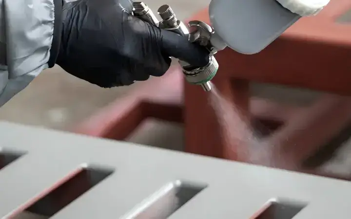 Worker applying rust-proof spray coating to metal sign frame in production facility