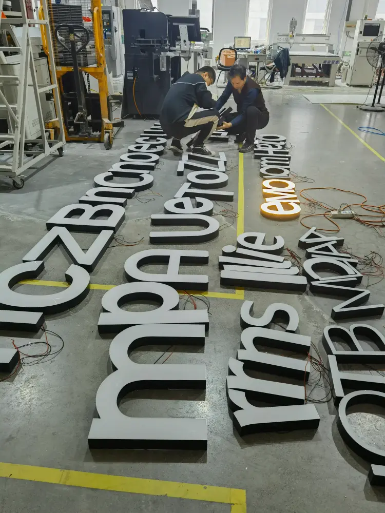 Factory workers inspecting large channel letters laid out on workshop floor with one letter lit for testing