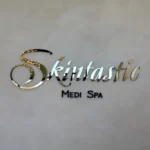 Reflective Skintastic Medi Spa acrylic logo with black lettering on a light wall