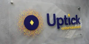 Uptick Entertainment sign with blue and yellow burst logo on textured wall