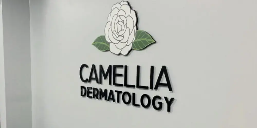 Camellia Dermatology sign with white flower and leaves logo icon on wall