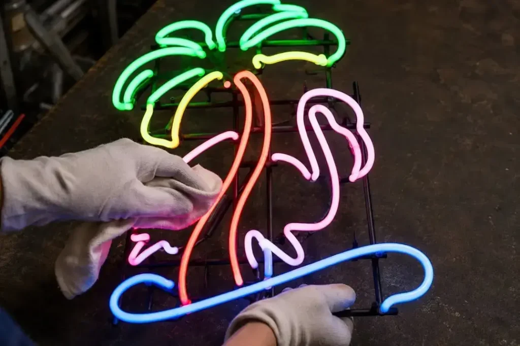 Worker cleaning and inspecting a colorful glass neon flamingo sign