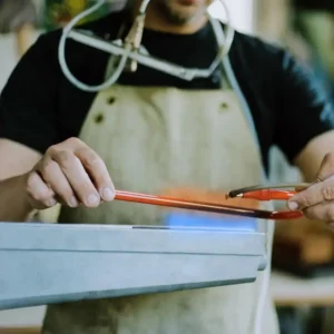 Neon artisan heating and bending a glass tube by hand over a flame