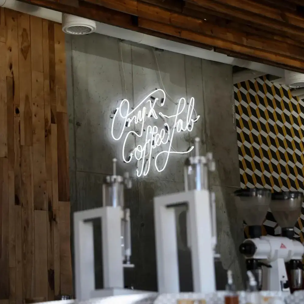 White real glass neon sign reading Onyx Coffee Lab on a concrete café wall