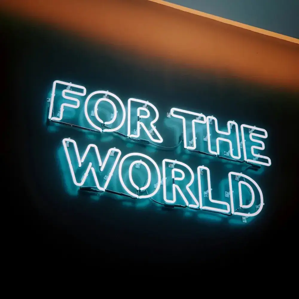 Turquoise real glass neon sign reading For the World on a dark wall