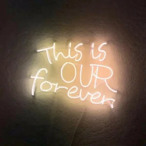 Warm white glass neon sign reading This Is Our Forever on a textured wall